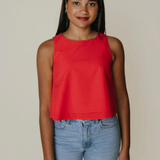 Woman wearing a red sleeveless top and blue jeans against a plain background