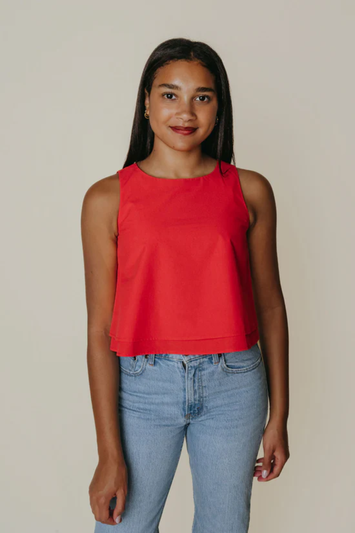 Woman wearing a red sleeveless top and blue jeans against a plain background
