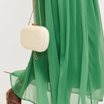 Person wearing a green dress and brown sandals holding a white woven handbag.