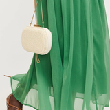 Person wearing a green dress and brown sandals holding a white woven handbag.