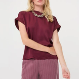 A woman modeling a short-sleeve burgundy top with a wide collar and matching mauve pinstriped trousers, accessorized with a chunky silver necklace, against a plain white studio background.