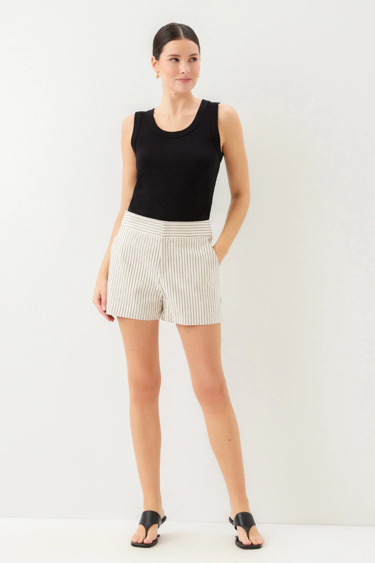 Woman wearing a black sleeveless top and white shorts on a plain background