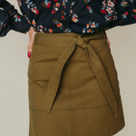 Person wearing a floral blouse and olive green skirt on a neutral background