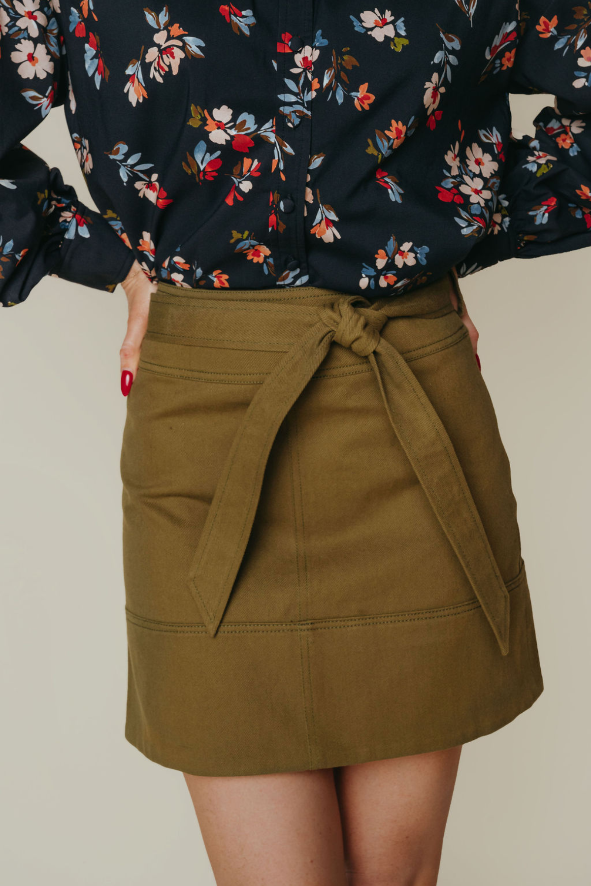 Person wearing a floral blouse and olive green skirt on a neutral background