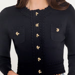 Black cropped cardigan with gold buttons worn by a person on a white background