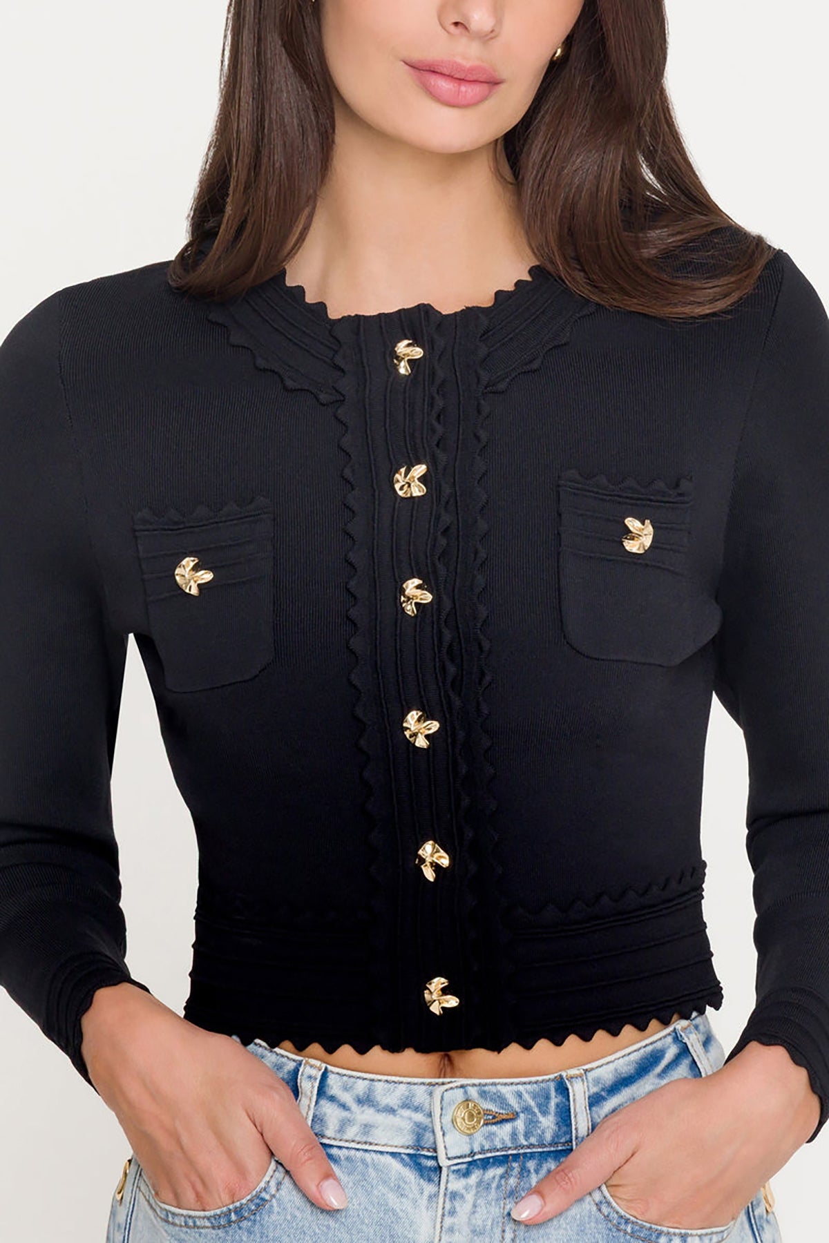 Black cropped cardigan with gold buttons worn by a person on a white background