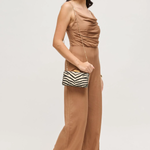 Woman wearing a brown jumpsuit holding a striped clutch against a white background