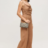 Woman wearing a brown jumpsuit holding a striped clutch against a white background