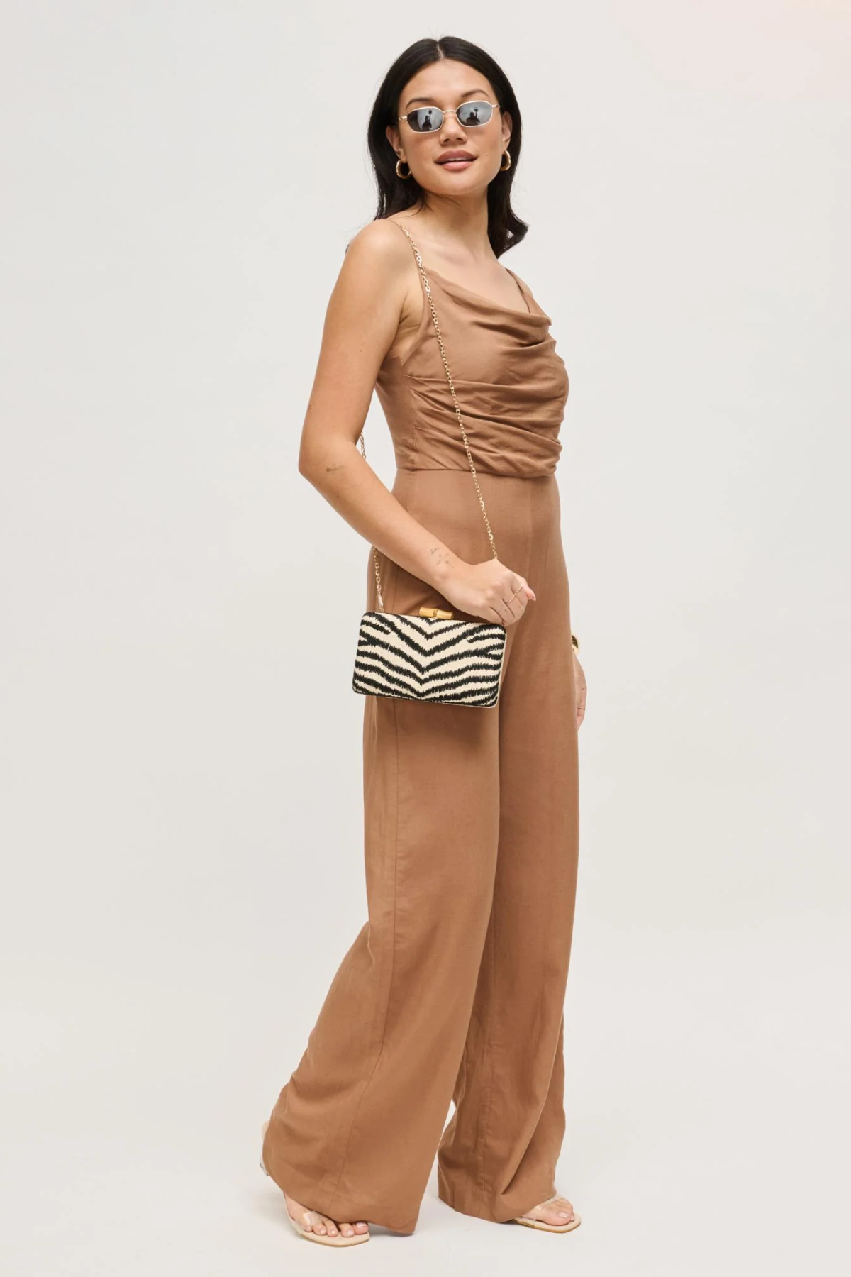 Woman wearing a brown jumpsuit holding a striped clutch against a white background