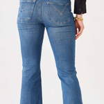 Rear view of a person wearing medium-wash blue flare jeans with a black top, standing against a plain light background.