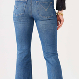 Rear view of a person wearing medium-wash blue flare jeans with a black top, standing against a plain light background.