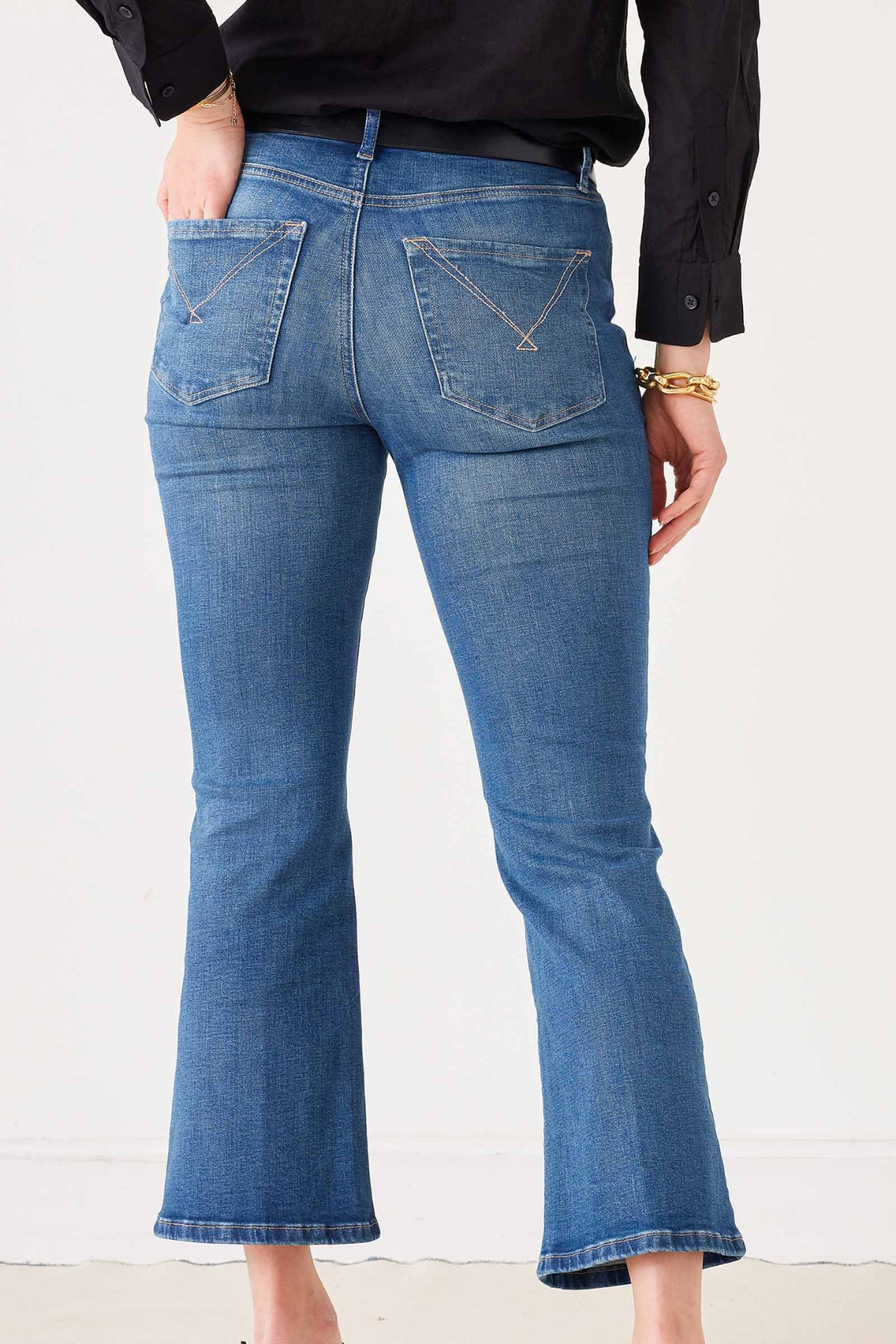 Rear view of a person wearing medium-wash blue flare jeans with a black top, standing against a plain light background.