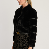 Woman wearing a black fur coat and leopard print pants on a plain background