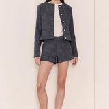 Woman wearing a jacket and shorts set with a white shirt on a plain background