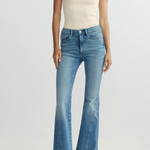 Person wearing a cream top and blue flared jeans on a white background