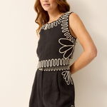 Woman wearing a black dress with white embroidery against a plain background