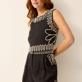 Woman wearing a black dress with white embroidery against a plain background