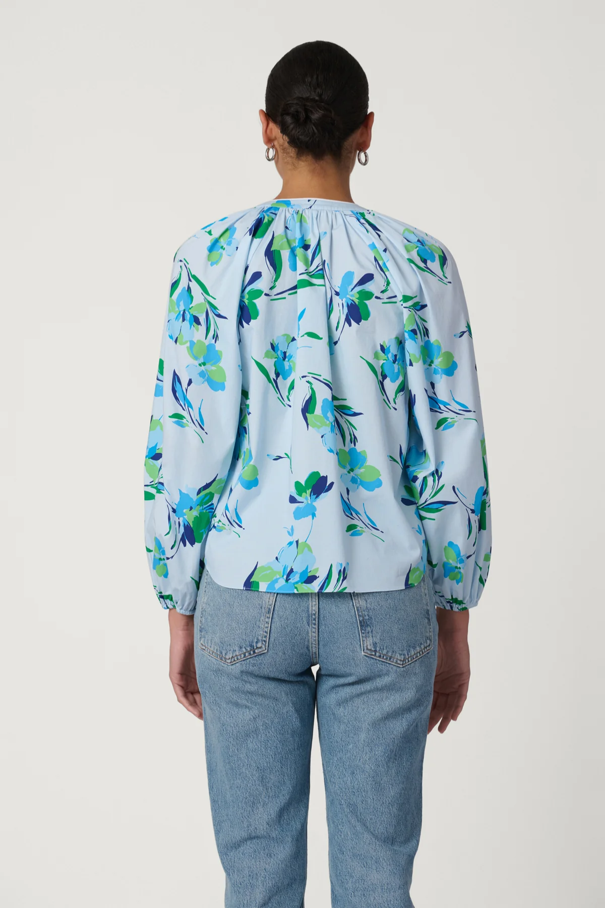 Person wearing a light blue floral blouse and jeans on a white background