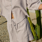 Person wearing a striped shirt and shorts standing next to a cactus plant.
