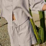 Person wearing a striped shirt and shorts standing next to a cactus plant.