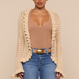 Woman wearing a beige crochet cardigan, brown top, and blue jeans on a beige background