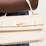 Beige handbag with gold accents held by a person wearing blue jeans.