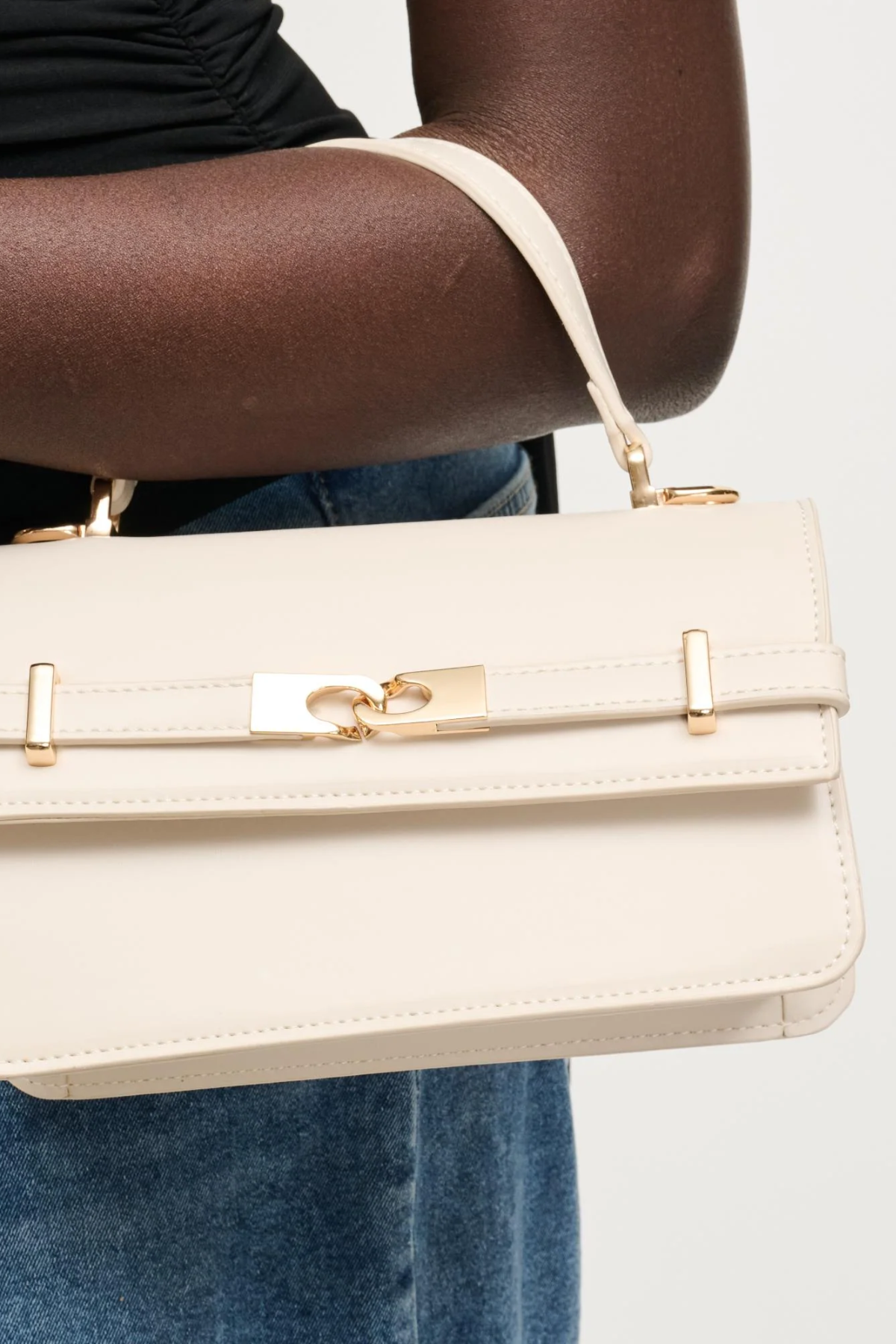 Beige handbag with gold accents held by a person wearing blue jeans.