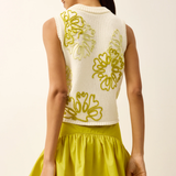 Woman wearing a white sleeveless top with yellow floral patterns and a yellow skirt on a light background