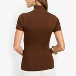 A woman shown from the back wearing a brown ribbed short-sleeve mock neck top and white pants against a plain light background.