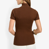 A woman shown from the back wearing a brown ribbed short-sleeve mock neck top and white pants against a plain light background.