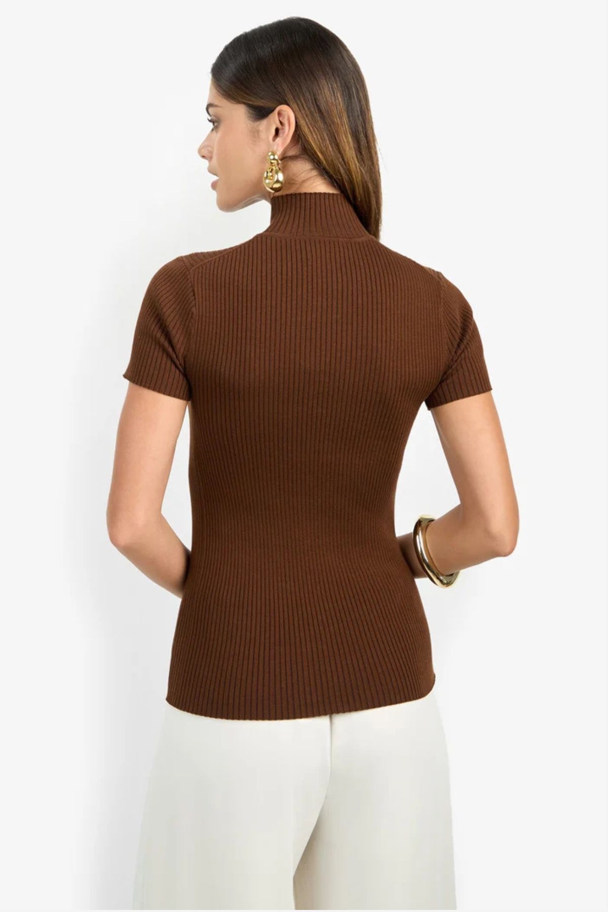 A woman shown from the back wearing a brown ribbed short-sleeve mock neck top and white pants against a plain light background.