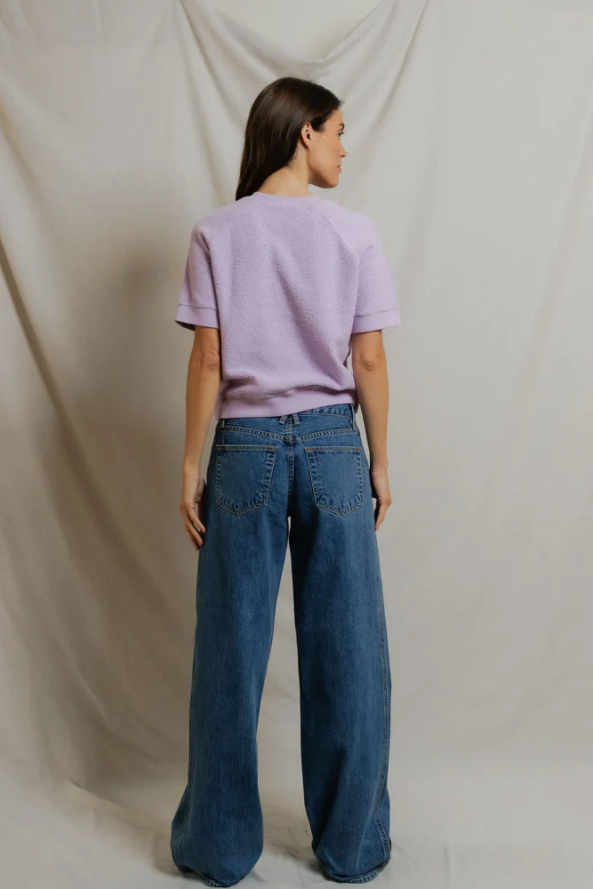 back of woman in short sleeve purple top on draped background 