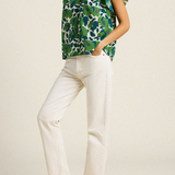 side of woman in green floral blouse on tan background 