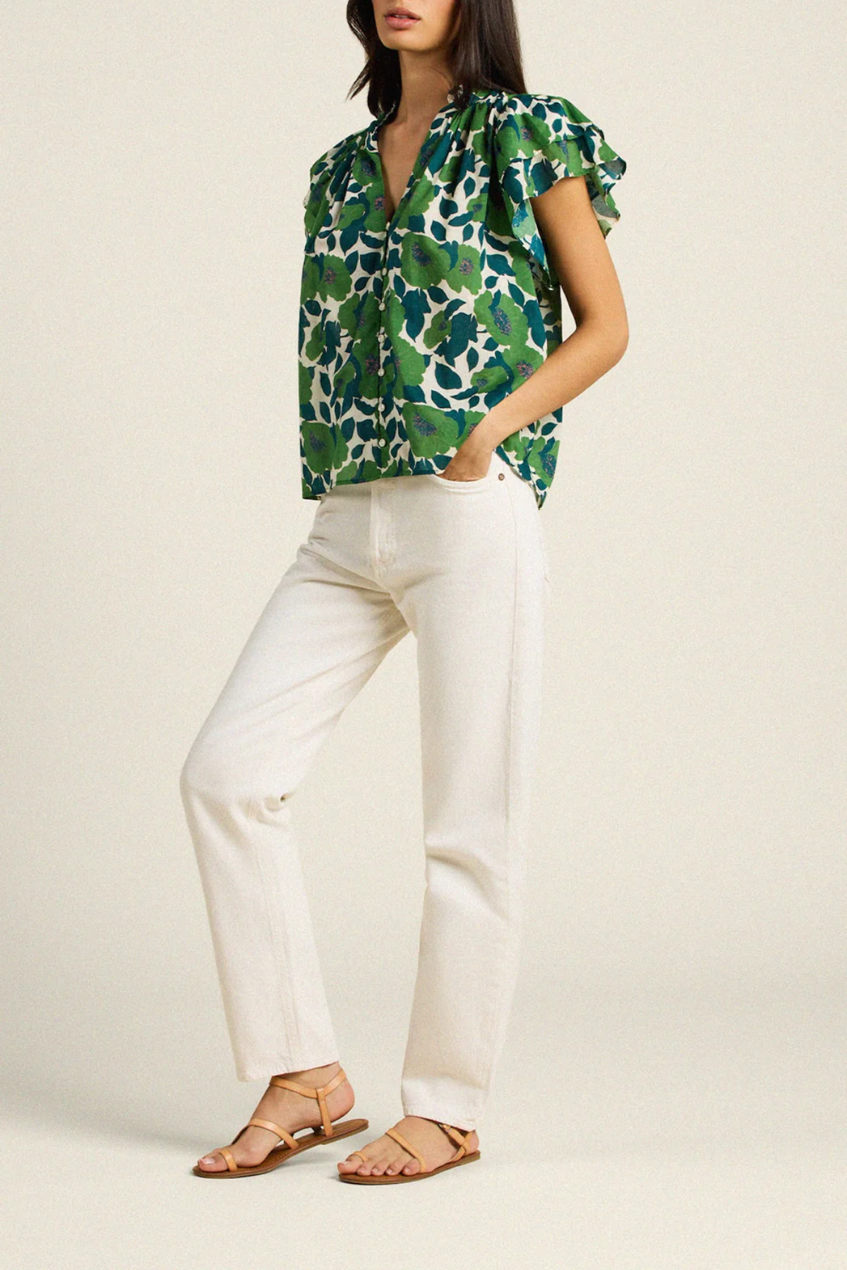 side of woman in green floral blouse on tan background 