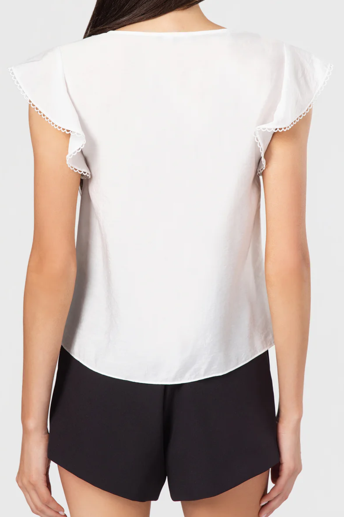 White blouse with lace trim and black shorts on a plain background