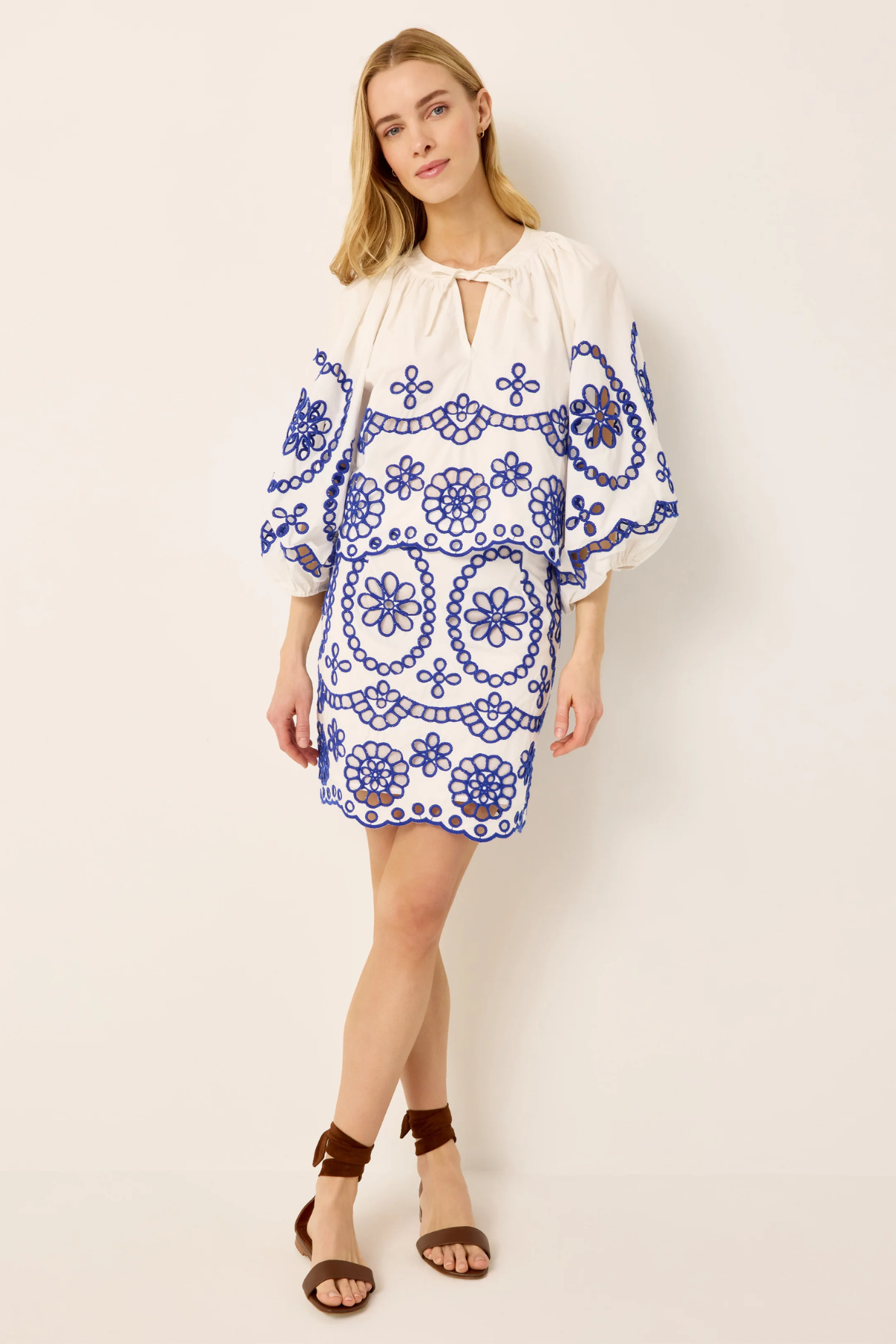 Woman wearing a white dress with blue floral embroidery on a plain background