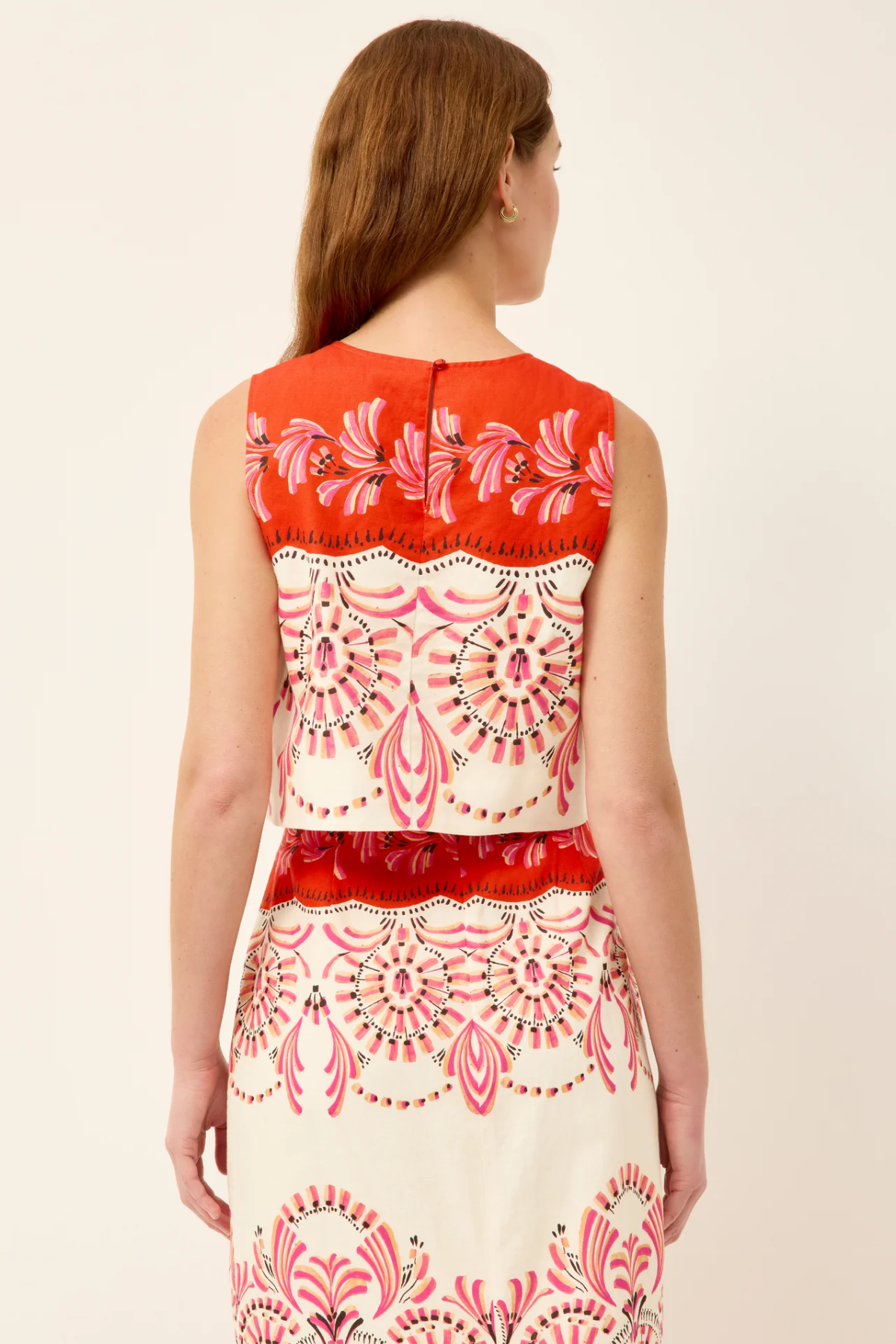 Woman wearing a sleeveless top with red and white floral pattern on a beige background