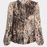 A long-sleeve blouse with a snakeskin print in shades of brown, beige, and black, featuring a ruffled round neckline and gathered sleeves, shown against a light gray background.
