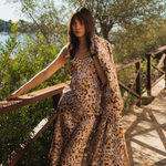 Woman in a leopard print dress standing on a wooden bridge with greenery and water in the background