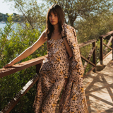 Woman in a leopard print dress standing on a wooden bridge with greenery and water in the background