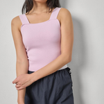 Woman wearing a light pink sleeveless top and dark pants against a plain background