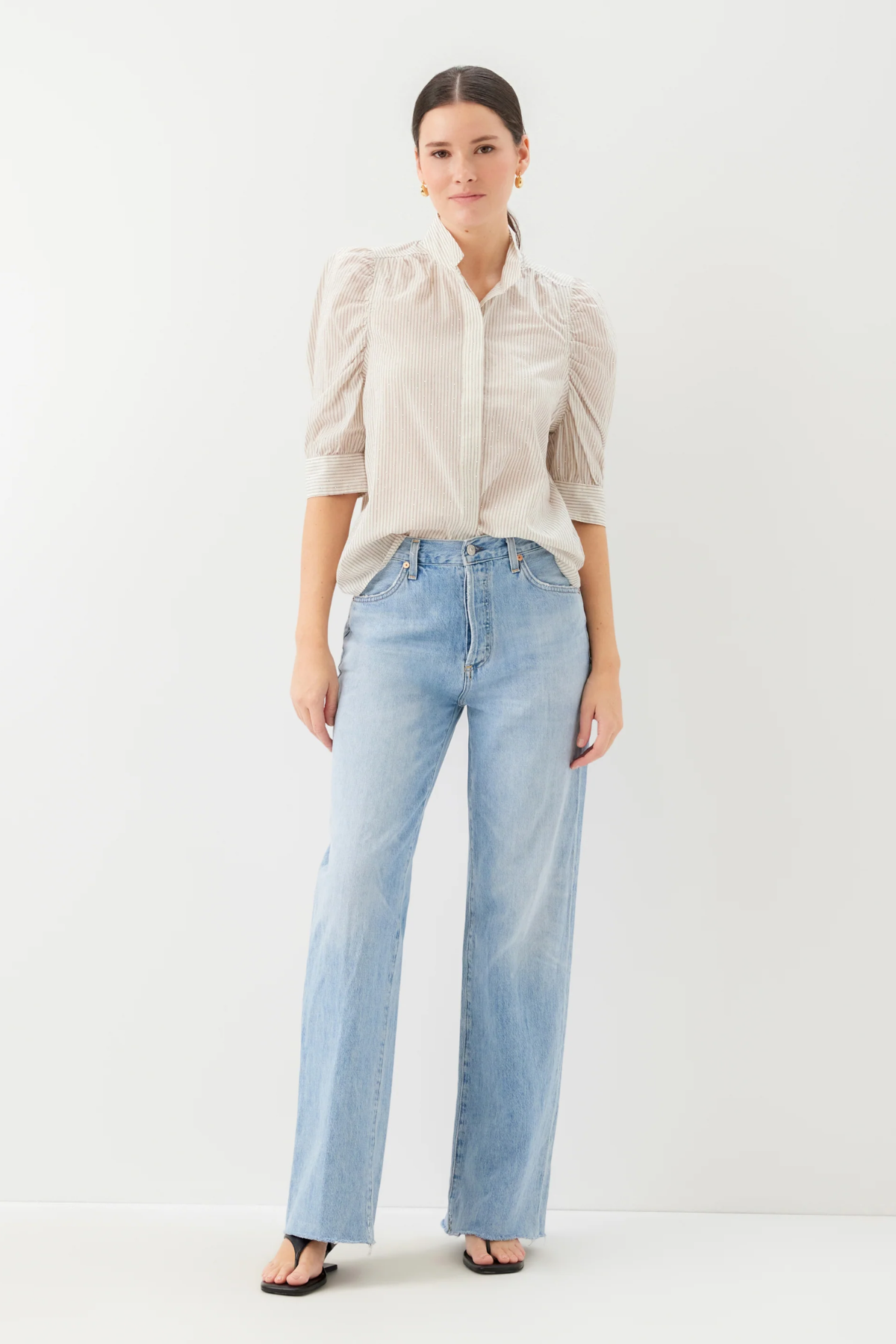 Woman wearing a beige blouse and light blue jeans on a white background