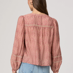 Woman wearing a pink floral blouse and blue jeans on a plain background
