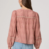 Woman wearing a pink floral blouse and blue jeans on a plain background