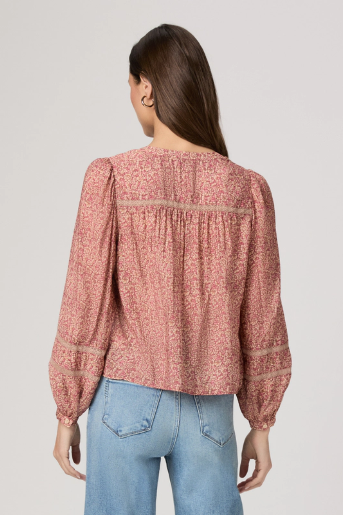 Woman wearing a pink floral blouse and blue jeans on a plain background