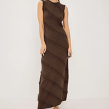 A woman modeling a sleeveless, high-neck, floor-length brown dress with diagonal textured fringe-like stripes, paired with black strappy heels, against a plain light gray studio background.