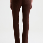 Rear view of a model wearing brown slim-fit jeans and black pointed-toe heels against a plain white studio background.