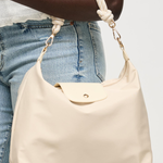 Beige handbag held by a person wearing blue jeans on a plain background