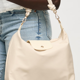 Beige handbag held by a person wearing blue jeans on a plain background