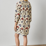 A woman modeling a cream-colored mini dress with a red and blue floral pattern, shown from a side-back angle against a neutral studio background.